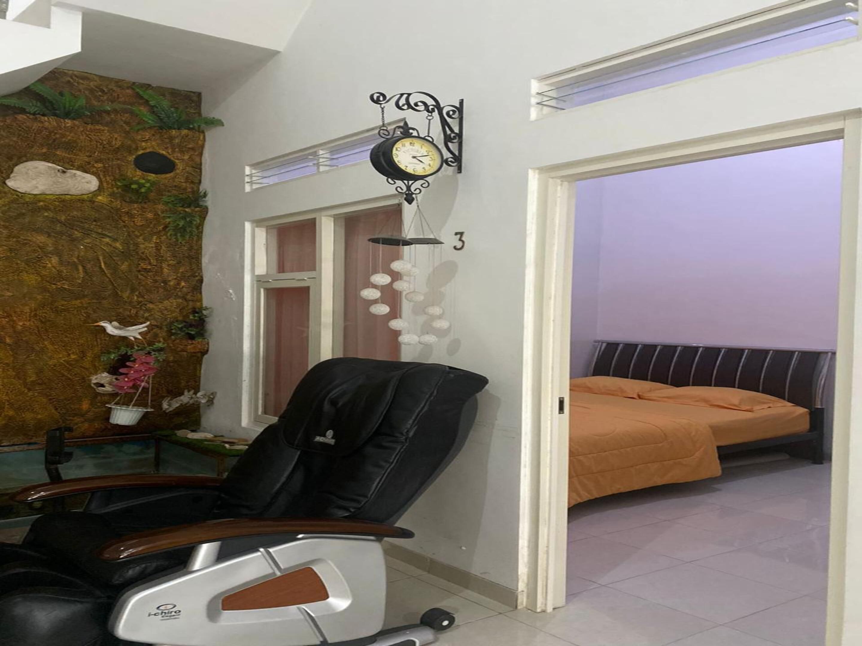 A room with a bed, a chair, a wall clock, and a door leading to another room.