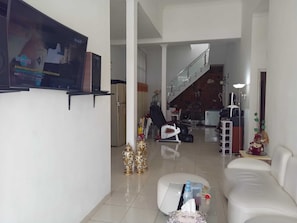 A living room with a sofa, a coffee table, a TV mounted on the wall, and a staircase leading to another level. - Cozzy Villa Rizka (Batu)