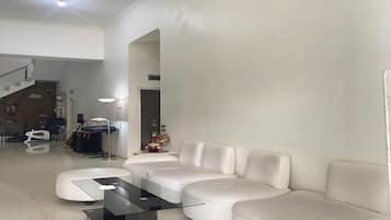 A modern living room with a glass coffee table, white leather sofa, and a staircase leading to another level.