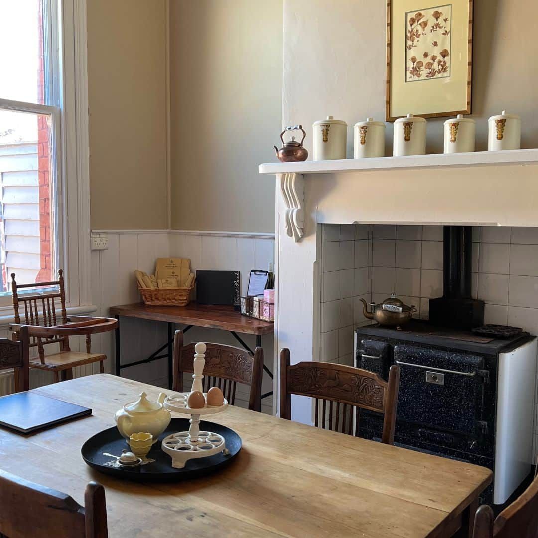 Une cuisine chaleureuse avec une cheminée, une table à manger avec des chaises et une bouilloire sur la cuisinière.