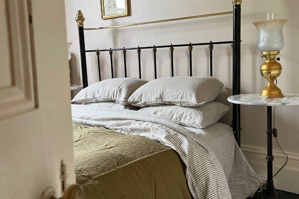 Un lit avec une tête de lit en métal, une table de chevet avec une lampe et un tableau encadré au mur.