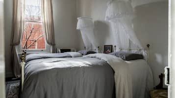 A bedroom with a large bed, a bedside table, a window with curtains, and a bedside lamp.