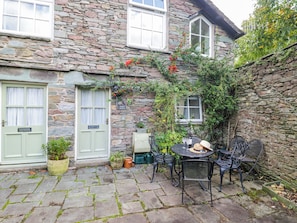 A stone house with a patio area featuring a table and chairs, a potted plant, and a small garden. - 2 Bakers Yard (Ambleside)