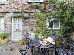 An outdoor seating area with a stone wall, a table with chairs, a bottle of wine, and a hat. - 2 Bakers Yard (Ambleside)
