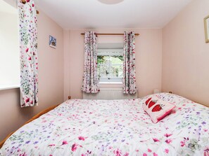 A bedroom with a floral bedspread, a window with curtains, and a bedside table with a pillow. - 2 Bakers Yard (Ambleside)