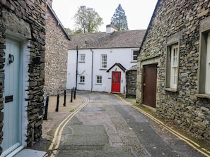A narrow street with stone walls, a red door, and a white building with multiple windows. - 2 Bakers Yard (Ambleside)