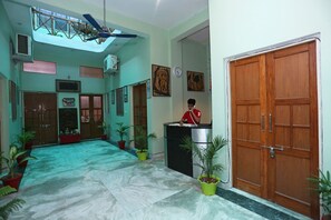 A hotel lobby with a reception desk, wooden doors, potted plants, and a ceiling fan. - Collection-O Sara Grand Near Ram (Lucknow)