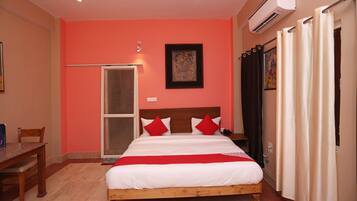 Habitación de hotel con cama, escritorio, silla, unidad de aire acondicionado y puerta.