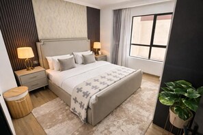 A modern hotel room with a large bed, bedside lamps, a potted plant, and a view of the outside. - Marina Bay Deluxe 2BR (Nairobi)