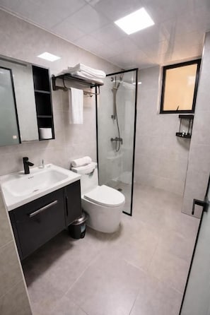 A modern bathroom with a glass shower enclosure, a white sink, and a toilet. - Marina Bay Deluxe 2BR (Nairobi)