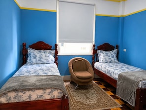 Ein Zimmer mit zwei Holzbetten mit passenden Kopfteilen, einem einzelnen braunen Sessel und einem gemusterten Teppich auf einem karierten Boden.