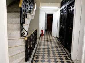 A hallway with a checkered floor, a staircase with black balusters, and a fire extinguisher. - Oscar Rodrigues 404 (São Paulo)