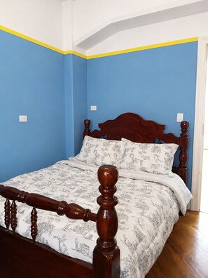 A bedroom with a wooden bed frame, a patterned bedspread, and blue walls. - Oscar Rodrigues 404 (São Paulo)