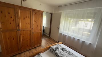 Una habitación con armario de madera, cama con ropa de cama estampada, ventana con cortinas de encaje y vistas al exterior.