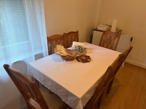 Una taula de dinar amb mantell blanc, caires de fusta, una cistella amb estesanes, un plat de sal i pebre, i un objecte decoratiu petit.
