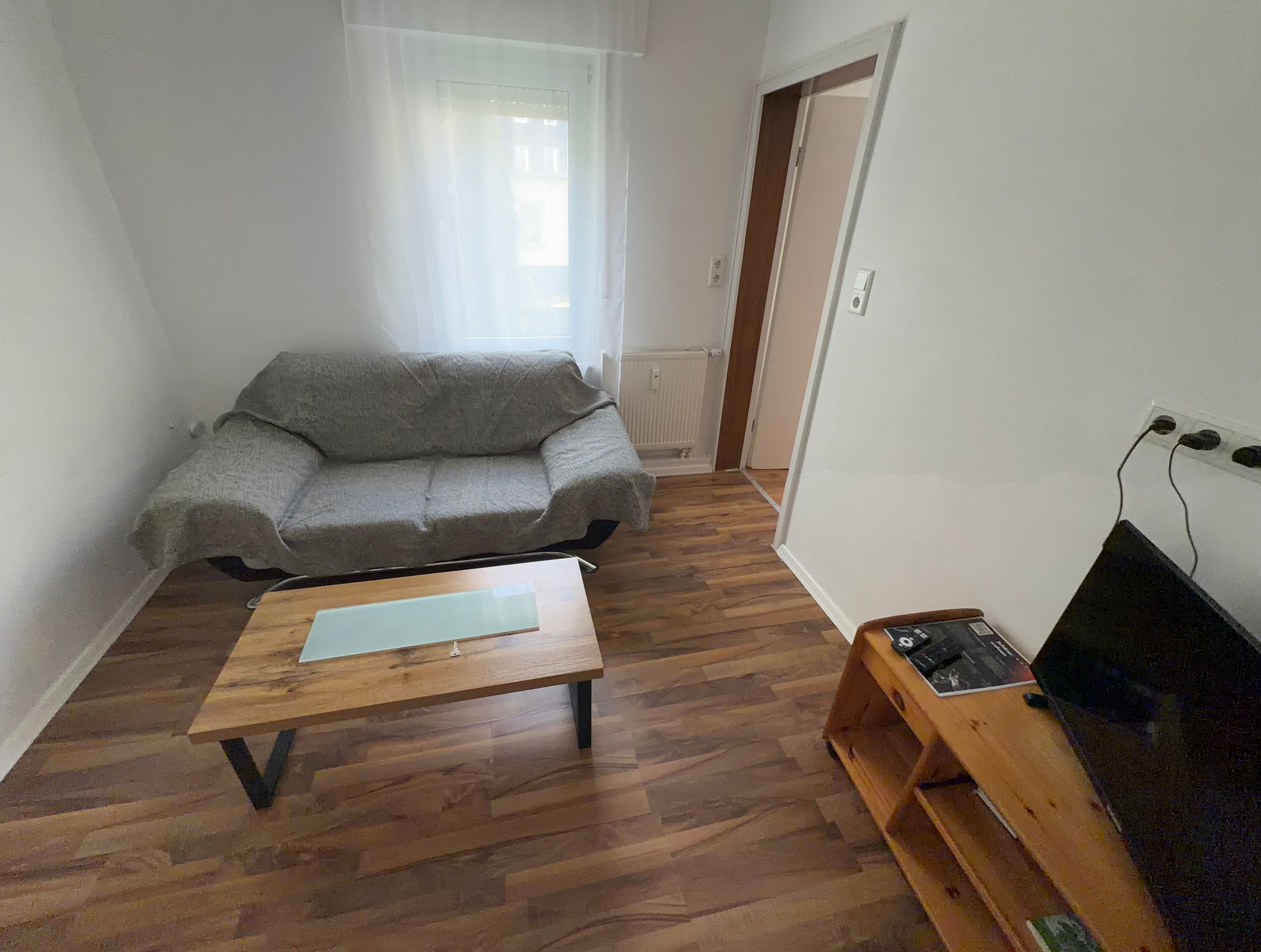 Ein Wohnzimmer mit grauem Sofa, einem Holztisch und einer TV-Konsole mit Flachbildfernseher.