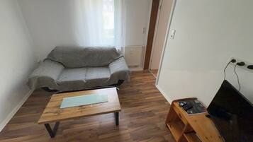 Ein Wohnzimmer mit grauem Sofa, einem Holztisch und einer TV-Konsole mit Flachbildfernseher.