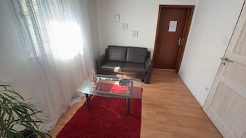 Ein Wohnzimmer mit einem Glastisch, einem roten Teppich, einem schwarzen Sofa und einer Holztür.