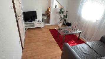 Ein Wohnzimmer mit Fernseher, einer Couch, einem roten Teppich und einer Treppe zu einem anderen Raum.