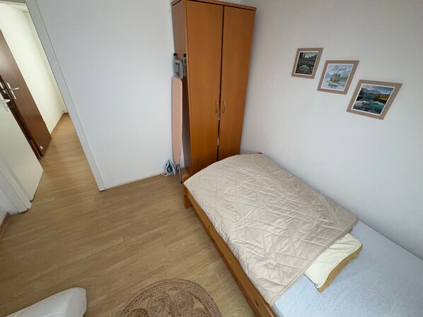 Ein Schlafzimmer mit einem Holzschrank, einem Bett mit gesteppter Matratze, einem kleinen Teppich und zwei gerahmten Bildern an der Wand.