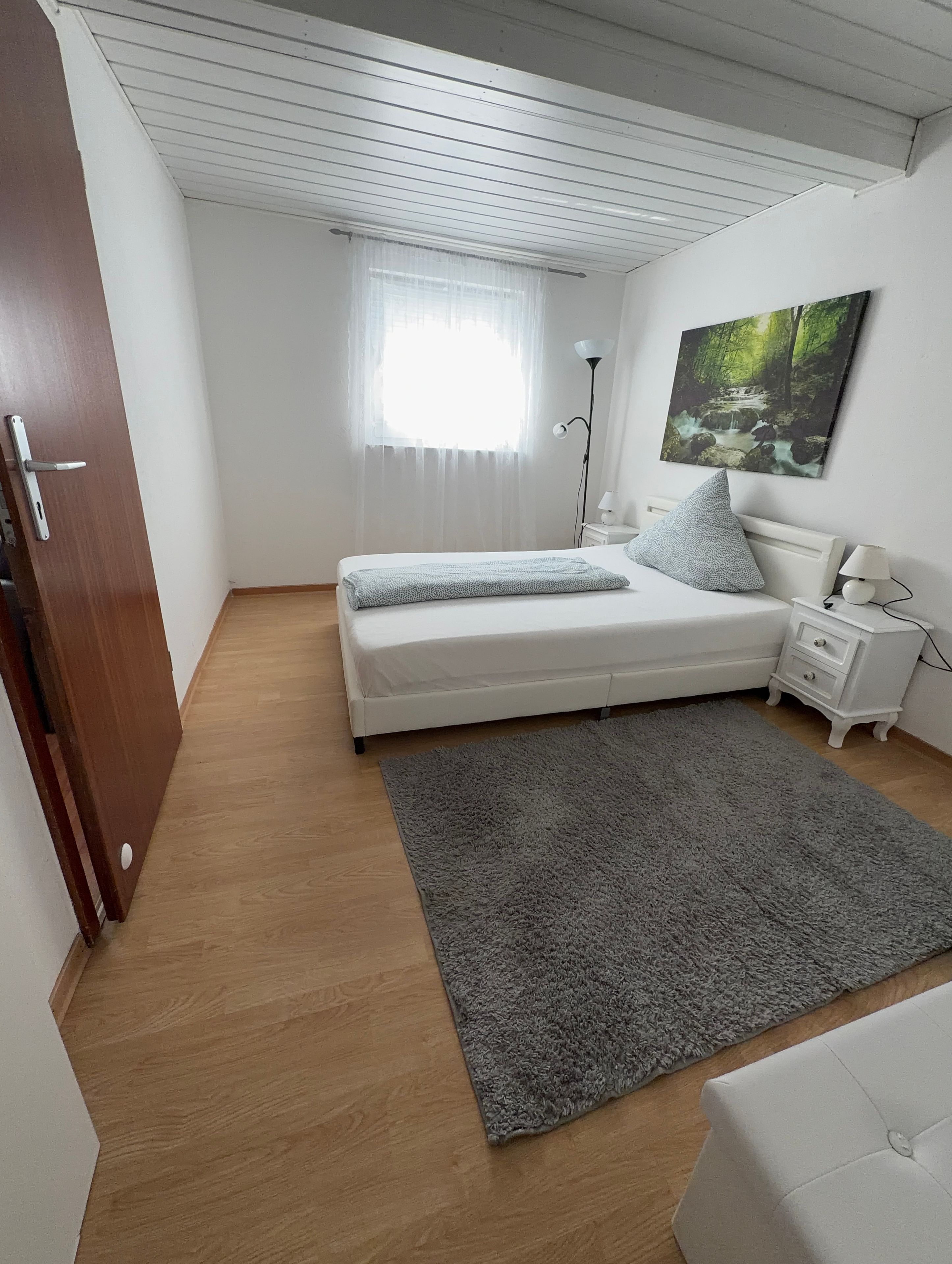 Un dormitorio con cama, mesita de noche, lámpara y un cuadro en la pared.