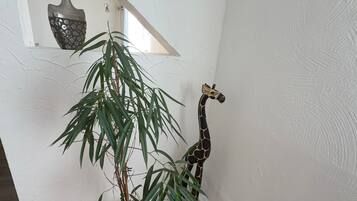 Ein Zimmer mit Holzboden, einer Topfpflanze, einem schwarzen Stuhl, einer weißen Wand und einer dekorativen Giraffe.