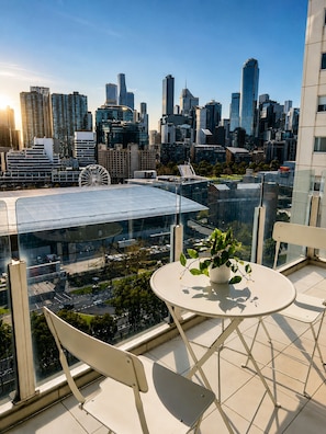 A cityscape view from a balcony with a table and chairs, a potted plant, and a Ferris wheel in the background. - Spectacular City Views | Large 3BR 2BA Near Crown & MCEC (Southbank)