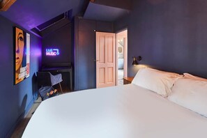 A bedroom with a bed, a door leading to a bathroom, and a neon sign indicating live music. - Tripps Mews | West Didsbury Mews House (Manchester)