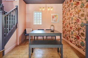 A dining area with a table, chairs, a bench, a vase, and a wall with floral wallpaper. - Tripps Mews | West Didsbury Mews House (Manchester)
