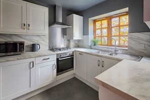A modern kitchen with white cabinets, a built-in microwave, a gas stove, and a window with stained glass. - Tripps Mews | West Didsbury Mews House (Manchester)
