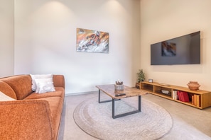 A modern living room with a sofa, coffee table, and a flat-screen TV mounted on the wall. - Newly Renovated 4-Bedroom Chalet - Mont Blanc Views, Hot Tub & Sauna (Chamonix-Mont-Blanc)