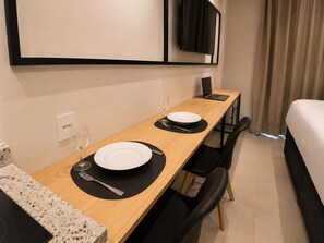 Ein Hotelzimmer mit Holztisch für zwei Personen, einem Laptop, einem Bett und einem an der Wand montierten Fernseher.