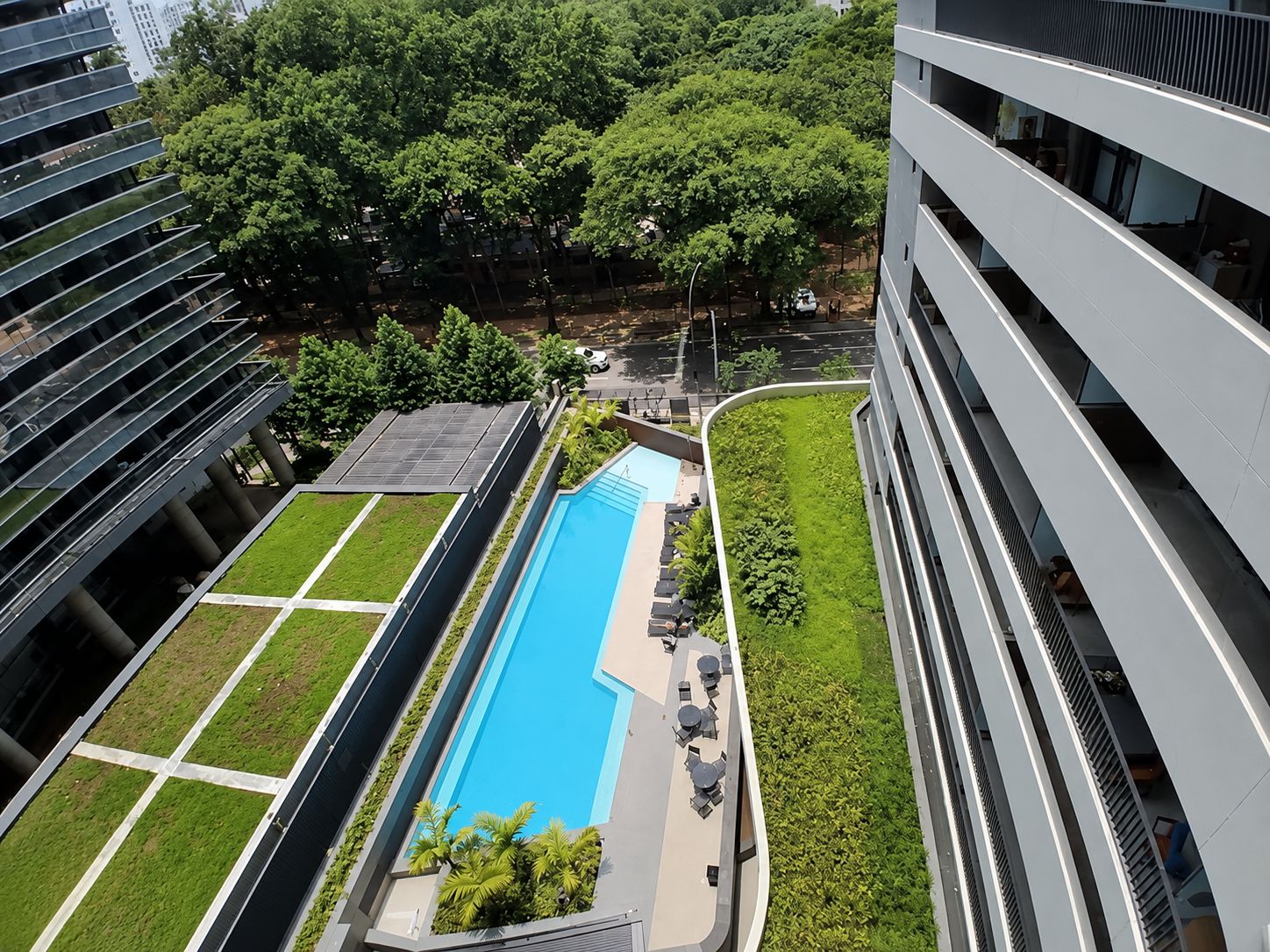 A modern building with a rooftop pool, surrounded by greenery and adjacent to other structures.