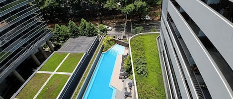 A modern building with a rooftop pool, surrounded by greenery and adjacent to other structures.