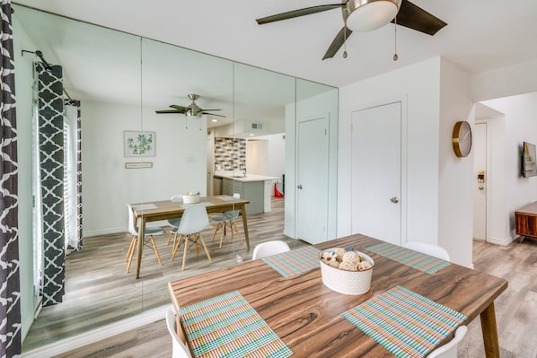 A modern dining area with a wooden table, white chairs, and a ceiling fan. - 2-bedroom condo in soothing Dallas with Pool, AC, Wifi, Parking, Washer (Dallas)