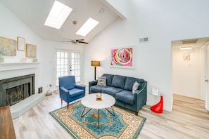 A living room with a fireplace, a blue armchair, a gray sofa, a round coffee table, and a colorful abstract painting on the wall. - 2-bedroom condo in soothing Dallas with Pool, AC, Wifi, Parking, Washer (Dallas)