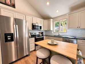 A modern kitchen with stainless steel appliances, a wooden island, and a view of greenery outside. - The Sunny Perch - Lakefront Home (Osage Beach)