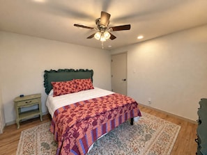 A bedroom with a bed, a nightstand, a ceiling fan, and a door. - The Sunny Perch - Lakefront Home (Osage Beach)