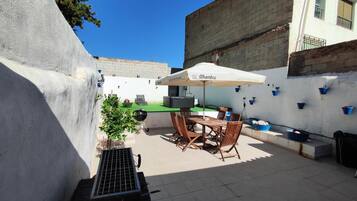 An outdoor patio with a table and chairs, a grill, and a potted plant.