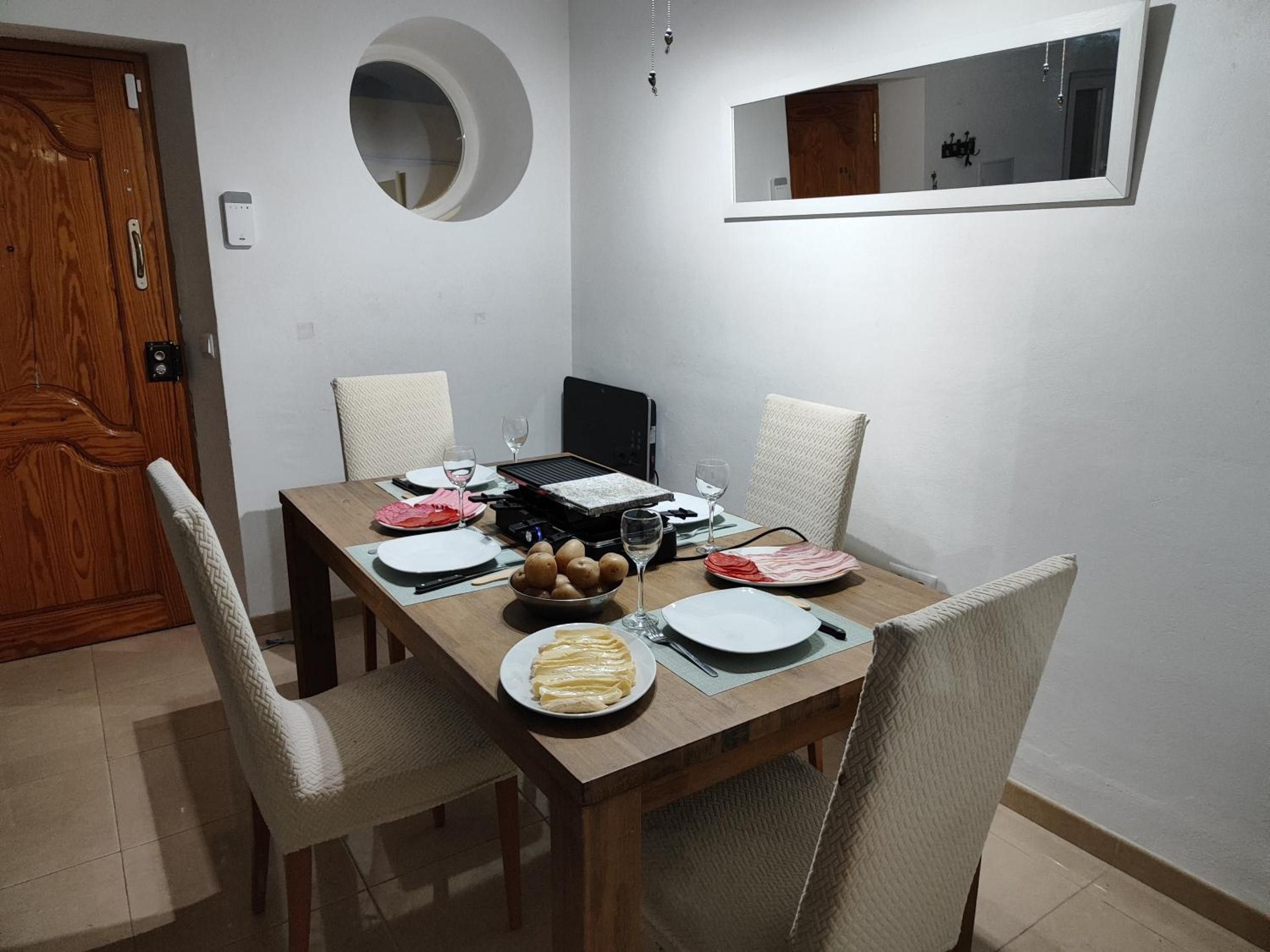 A dining area with a wooden table set for four, including plates, cutlery, and a bowl of potatoes.