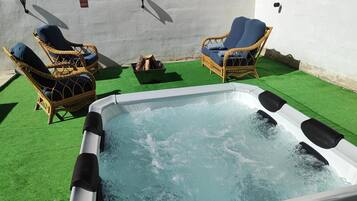 A hot tub with two wicker chairs and a fire pit on a green artificial lawn.