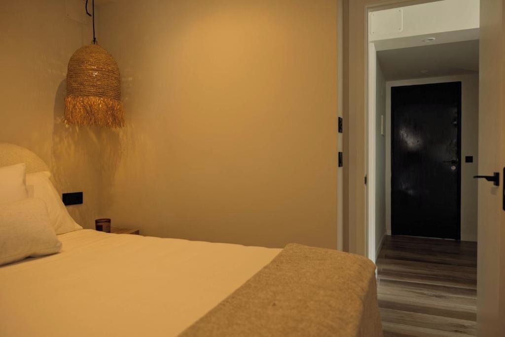 Een hotelkamer met een bed, een hanglamp en een deur naar een andere kamer.