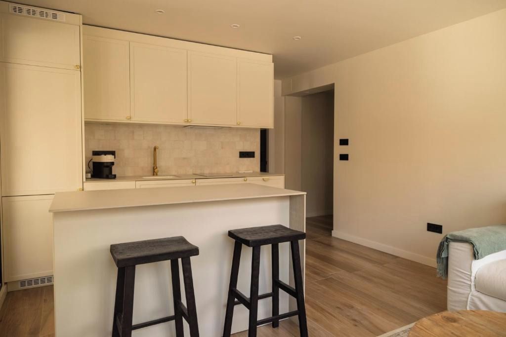 Cozinha moderna com armários brancos, bancada e dois bancos.