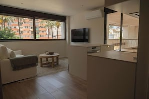 Een moderne woonkamer met een bank, een klein rond tafeltje en een flatscreen televisie die aan de muur is bevestigd.