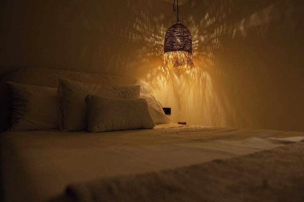 Een kamer in gedempt licht met een bed, kussens en een hanglamp.