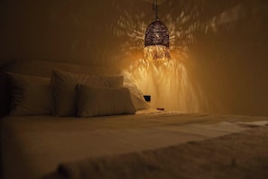 Een kamer in gedempt licht met een bed, kussens en een hanglamp.