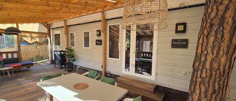 Eine überdachte Terrasse im Freien mit Tisch und Stühlen, Holzbalken und einer hängenden Leuchte.