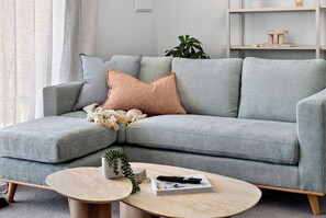 A modern living room with a grey sectional sofa, a round coffee table, and a potted plant. - Coastal Views – Mosman Park – 2BR with Balcony & Pool (Mosman Park)