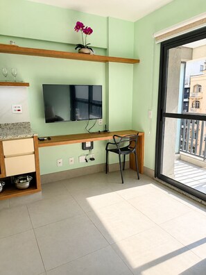 A modern room with a flat-screen TV, a wooden desk, a chair, and a balcony with a view of buildings. - SETIN 806 (São Paulo)