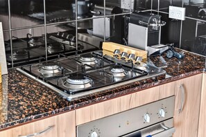 A kitchen with a four-burner gas stove, stainless steel appliances, and a granite countertop. - Wellington Breeze – Mosman Park – 2BR with Pool & Balcony (Mosman Park)